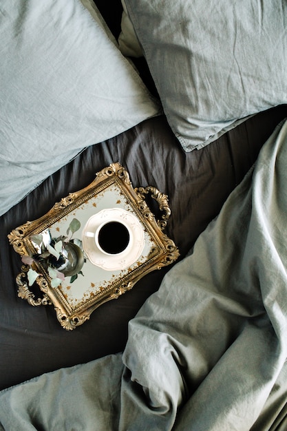 'S ochtends koffie op gouden vintage dienblad in bed met grijs laken en kussens