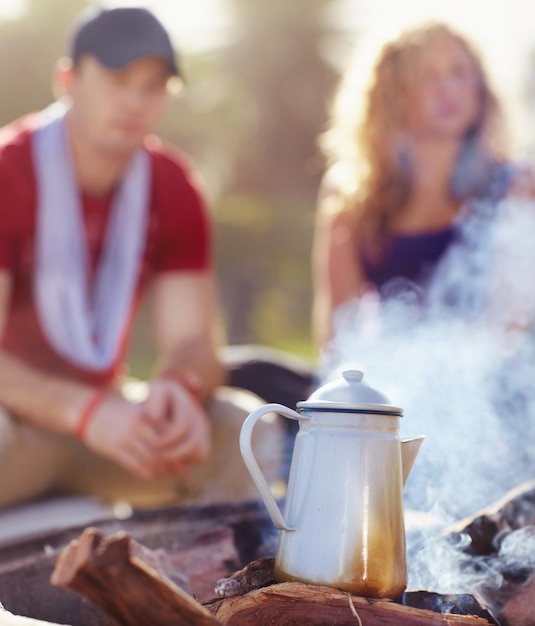 's ochtends koffie op het brouwsel koffie staat op een kampvuur buiten met een jong stel op de achtergrond