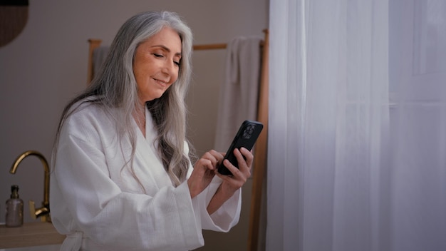 S old caucasian senior mature woman grandmother lady standing in bathroom in bathrobe looking at