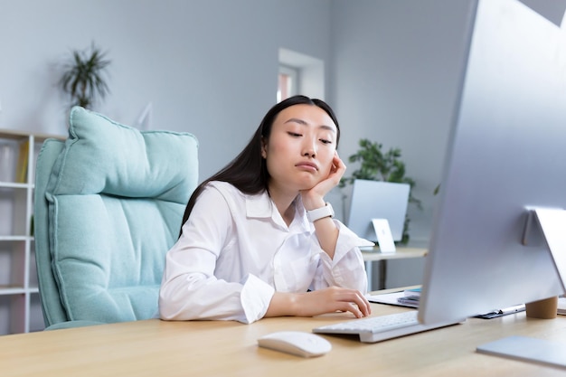 Saai en eentonig werk een jonge mooie aziatische zakenvrouw een kantoormedewerker zit aan een bureau bij