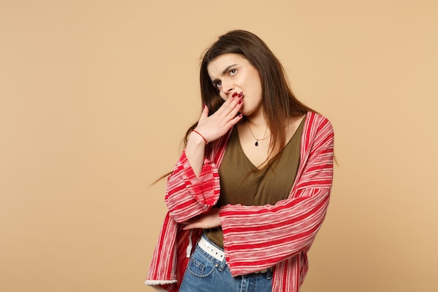 Saaie jonge vrouw in casual kleding opzoeken, geeuwen, die mond bedekken met hand geïsoleerd op pastel beige muur achtergrond in studio. Mensen oprechte emoties, lifestyle concept. Bespotten kopie ruimte.