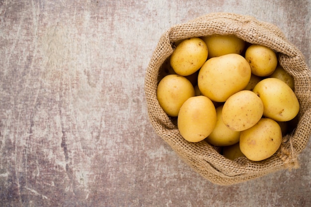 Sack of fresh raw potatoes on wooden background, top view.