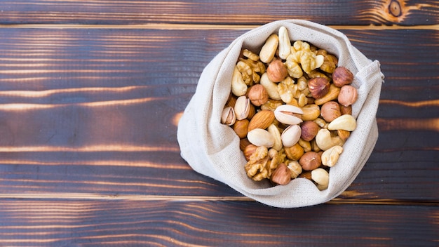 Sack with different nuts on wooden background