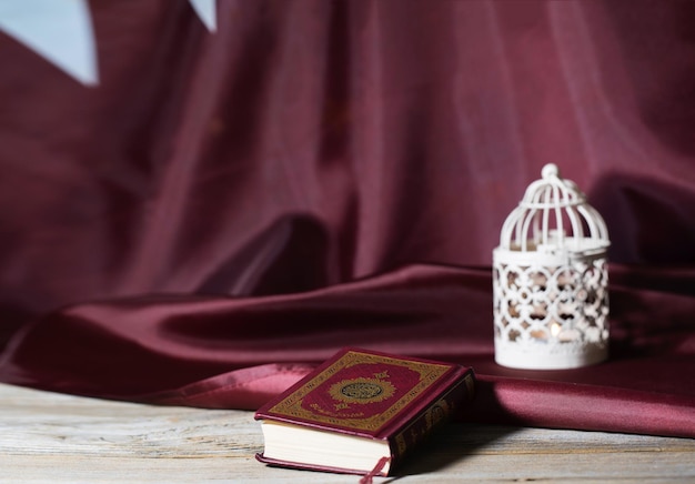 Sacred book of Quran on a wooden surface Flag of Qatar and candle holder in the background Tanslation the book contains verses of Koran