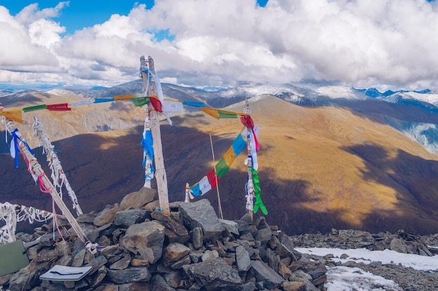 Sacred shamanic stone pile decorated with colored ribbons on the top of the mountain pass with mountain valley picturesque view Marvelous mountain range Altai mountains