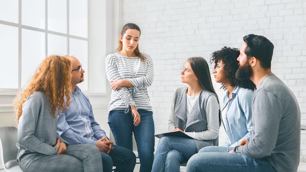 Sad addicted woman sharing her problems at rehab group meeting