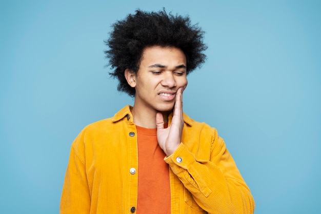 Sad African American man holding hand on his cheek having a toothache. Dental care concept