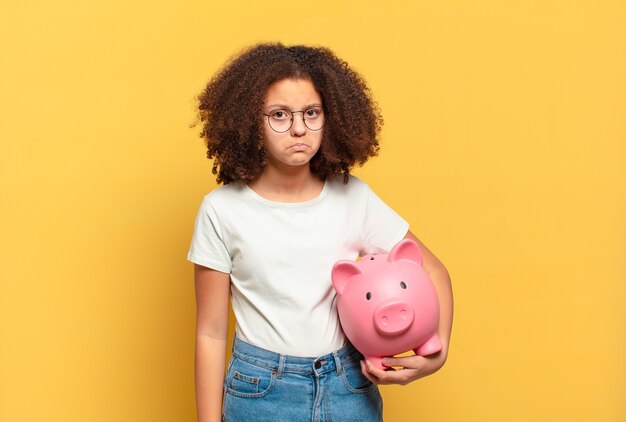 Sad afro teenager with piggy bank. savings concept