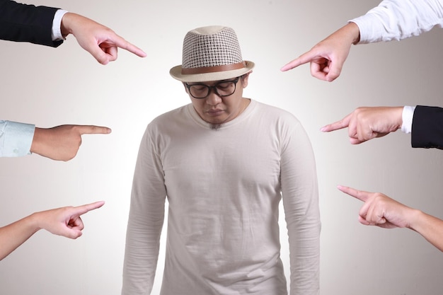 Sad anxious Asian man judged by different hands Concept of accusation of guilty person