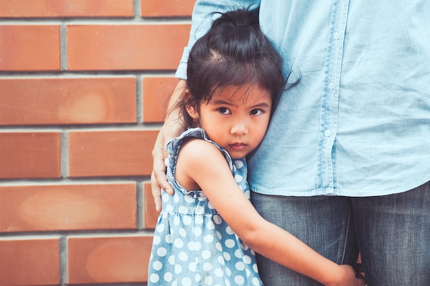 Foto ragazza asiatica triste del bambino che abbraccia la sua gamba della madre