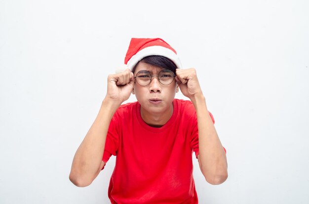 Грустный привлекательный азиатский мужчина в красной рождественской одежде с грустным выражением лица вытирает слезы.