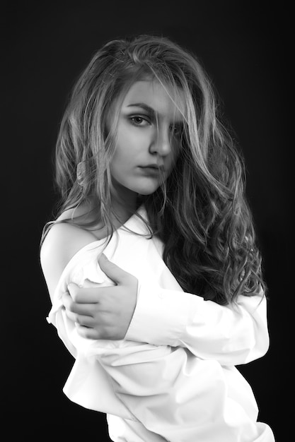 Sad attractive woman wears men's shirt posing in the shadows at studio. Black and white image