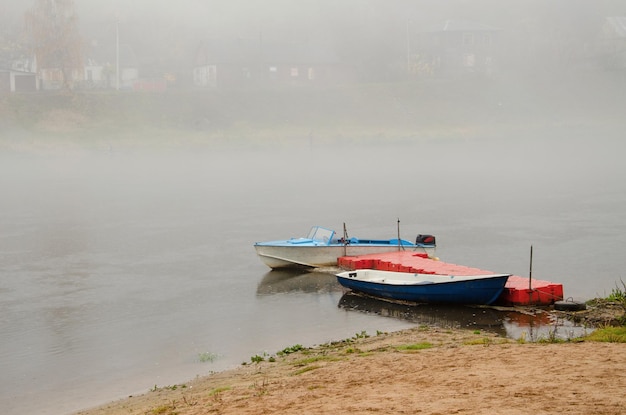 Sad autumn landscape fog and rain over the river rescue boats\
stand at the shore walk on the water in bad weather two boats\
moored at the river dock