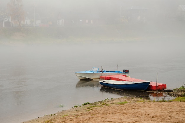 Sad autumn landscape Fog and rain over the river Rescue boats stand at the shore Walk on the water in bad weather Two boats moored at the river dock