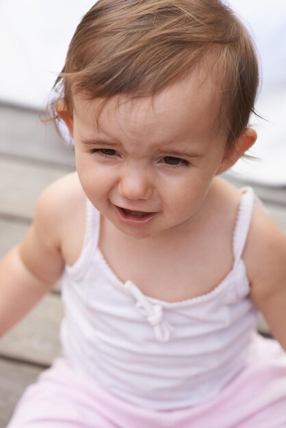 Sad baby face and sitting outside of curious toddler little girl or disappointed on outdoor porch Closeup of young unhappy child upset kid or adorable cute newborn with frowning facial expression