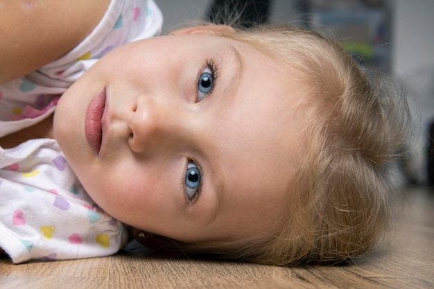 Triste bella bambina in una maglietta sdraiata su un pavimento di legno