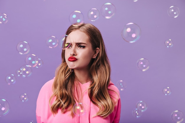 Sad blonde woman posing on purple wall with bubbles