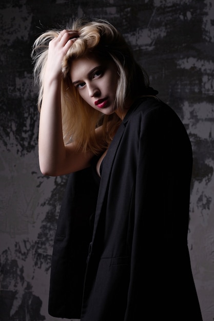 Sad blonde woman wearing jacket and bra posing at studio with shadows