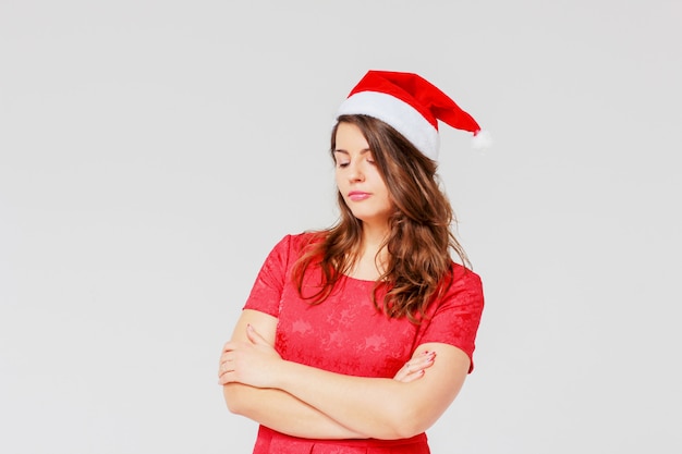 Sad body positive charming beautiful girl brunette in red dress and Santa hat on gray back