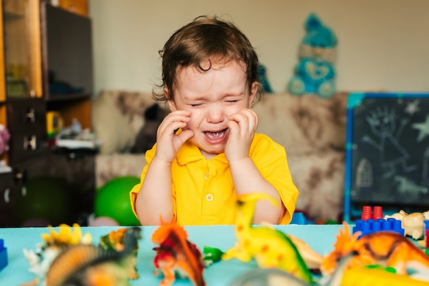 Грустный мальчик плачет рядом с игрушечными динозаврами