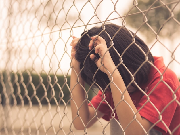 Sad boy behind fence mesh netting. Emotions concept - sadness, sorrow
