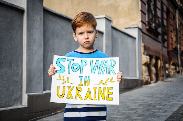 도시 거리에서 Stop War In Ukraine라는 단어가 적힌 국기 색깔의 포스터를 들고 있는 슬픈 소년