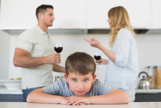 Ragazzo triste che si appoggia sul tavolo mentre i genitori discutono