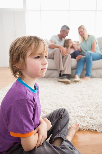 両親が姉妹と一緒に楽しんでいる間に床に座っている悲しい少年