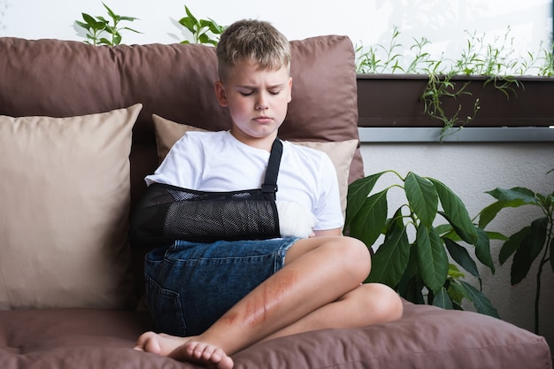 Sad boy with a broken arm and wounds on his leg gypsum on a childs hand