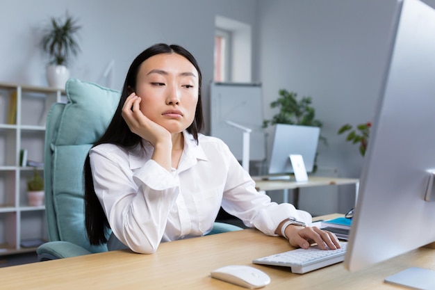 A sad business woman works in a modern office an asian woman thinks about the results of work