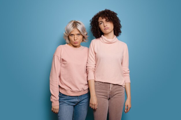 Sad caucasian women with curly hair and same clothes posing on a blue  wall