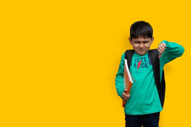 Photo sad child boy with books in hand and bag on shoulders, hate study concept copy space