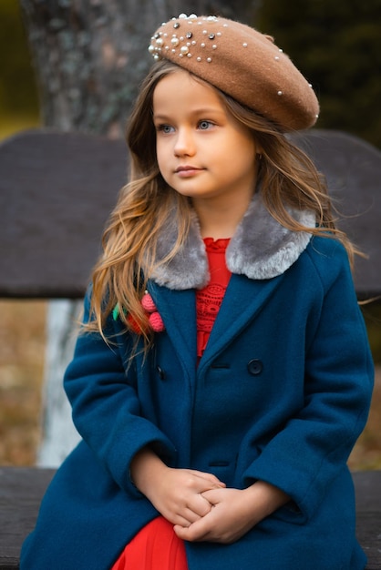 Sad child sitting on a park bench in old fashion clothes