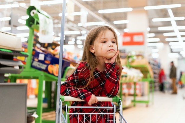 Грустный ребенок стоит за тележкой и выбирает продукты домой. Пустые полки в магазинах, пандемия и истерия из-за коронавируса