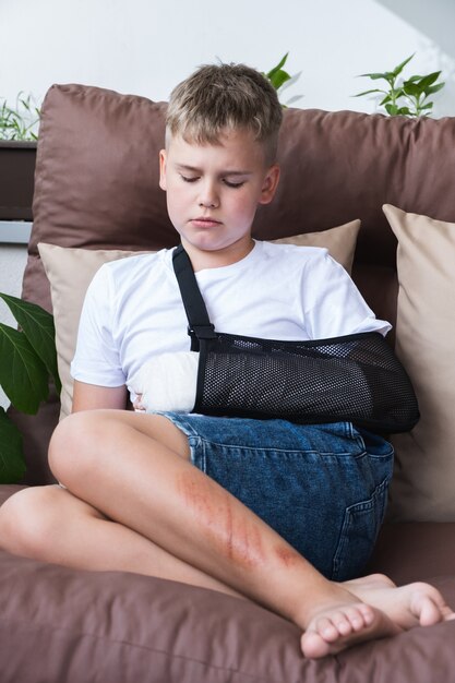 Sad child with a broken arm in home environment cast on hand of\
little boy