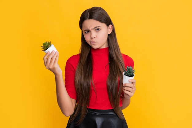 Sad child with cactus plant in pot on yellow background