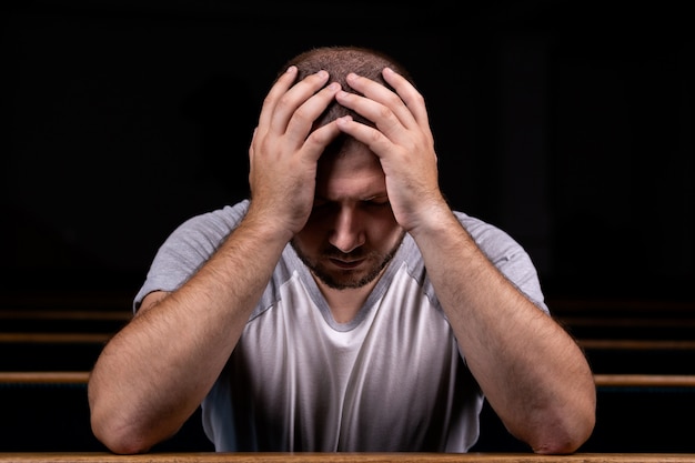 A Sad Christian man in white shirt is sitting and praying with humble heart in the church