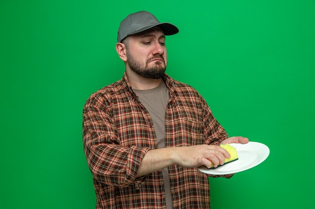 Sad cleaner man cleaning plate with sponge 