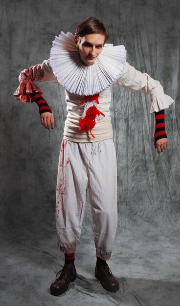 Фото Печальный клоун из фильма ужасов в белом костюме с красными помпонами и брызгами крови