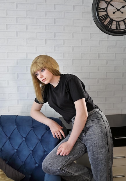 A sad concentrated girl teenager stands next to armchair clock on wall