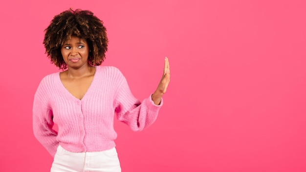 Sad confused millennial african american curly woman in casual show hand stop sign isolated on pink background