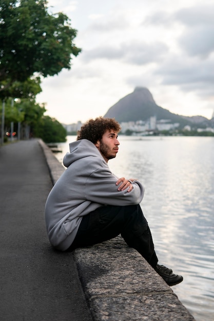 Foto uomo triste e contemplativo seduto in riva al lago