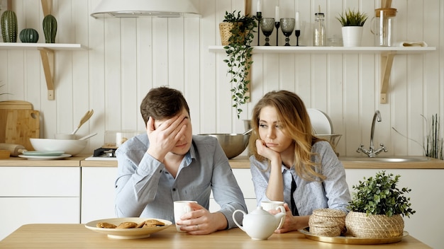 Sad couple girl guy have breakfast drinking tea silently