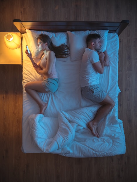 The sad couple with smartphone lay on the bed. night time. view from above