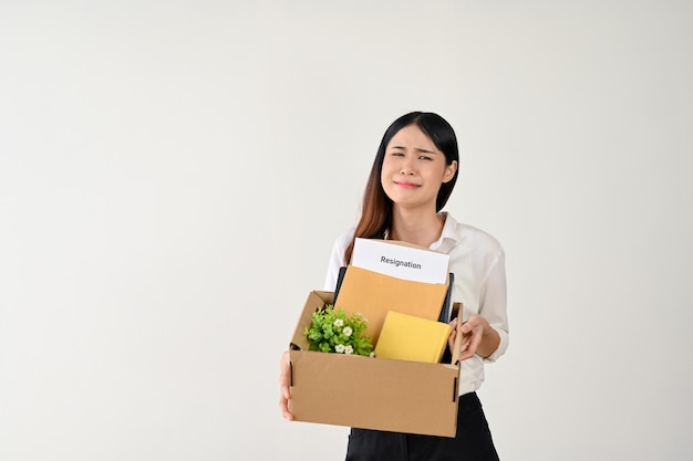 A sad and crying Asian female office worker is carrying a cardboard box with her resignation letter