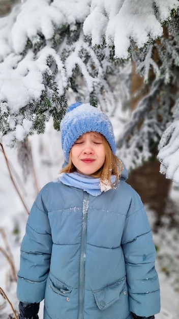 雪に覆われたトウヒの下で青いコートを着た悲しいかわいい女の子