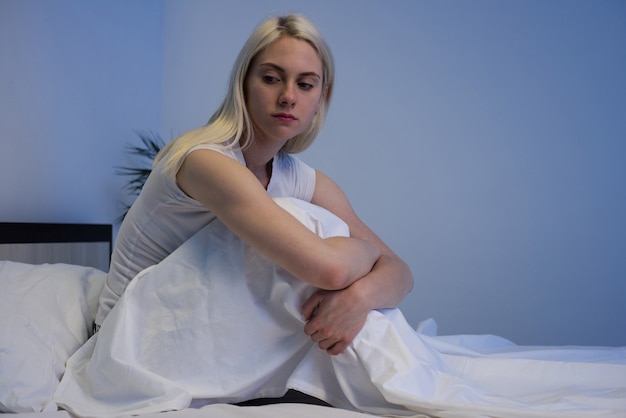 Sad depressed woman sitting in her bed late at night, she is pensive and suffering from insomnia - Image