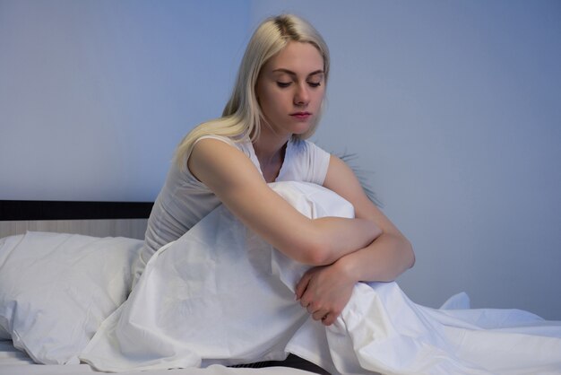 Sad depressed woman sitting in her bed late at night, she is pensive and suffering from insomnia