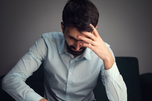 A sad and depressed young man is sitting on a sofa