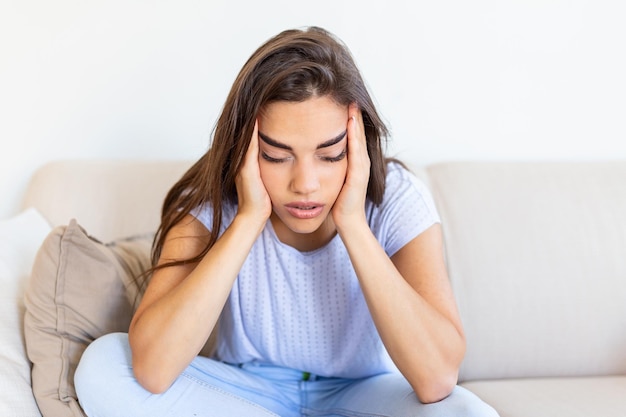 Sad and depressed young woman sitting on a couch in the living room at home